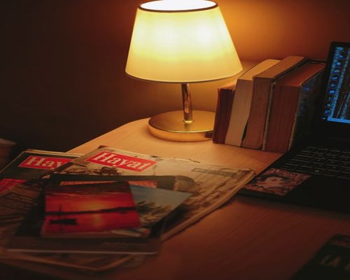 A modern soft desk lamp illuminating an open physical paper book on a comfortable table layout next to a window view